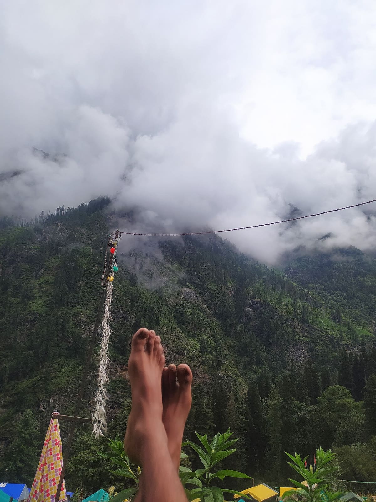 Feet resting on a cliff-edge swing above a deep cloud-filled Himalayan valley